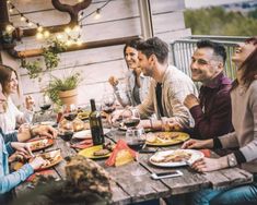 a group of people sitting around a wooden table eating food and drinking wine at the same time