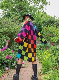 a woman standing on a brick path wearing a multicolored crocheted coat