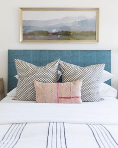 a bed with two pillows on top of it and a painting above the headboard