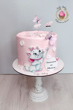 there is a pink cake with white cats and butterflies on the top, it's frosting has been made to look like a cat