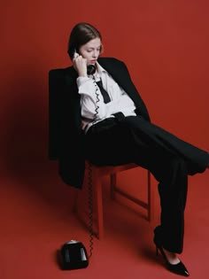 a woman sitting in a chair while talking on the phone and holding a telephone to her ear