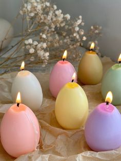 six candles are lined up in pastel colors on wax paper next to some flowers