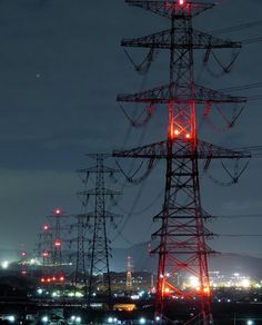 an electrical tower lit up at night with the city lights in the backround