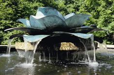 a large metal flower fountain in the middle of a pond with water flowing from it