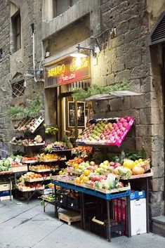 an outdoor market with fruits and vegetables on display in front of a stone wall building