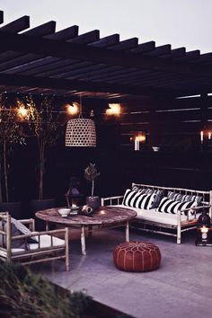 an outdoor living area with couches, tables and lights hanging from the rafters