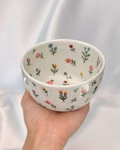 a hand is holding a white bowl with flowers on it and the bottom has a flower pattern