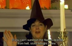 a woman wearing a witches hat standing in front of a candle with her hands up