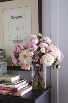 pink flowers in a vase sitting on a table next to books and a framed painting