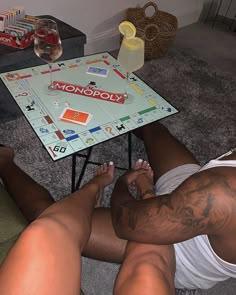 two men sitting on the floor playing monopoly with their legs crossed and one man has tattoos on his chest