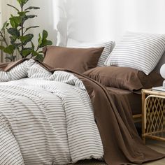 a bed covered in brown and white striped linens next to a plant with green leaves