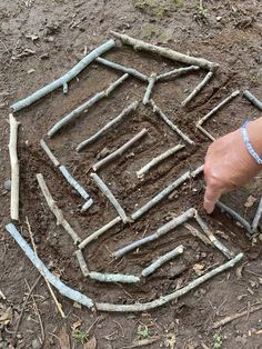 a hand pointing at an arrangement of sticks in the ground with one finger on it