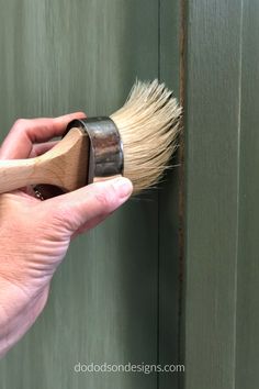 a hand holding a paint brush in front of a green painted wooden door with brown trim