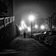 a black and white photo of cars parked on the side of a road at night