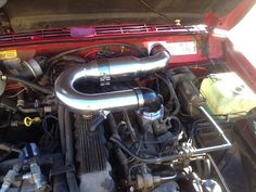 the engine compartment of a red car with its hood up and it's hoses out