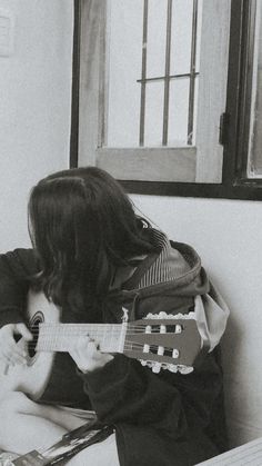 a person sitting on a couch with a guitar in their lap and looking out the window