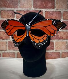 This stunning, handmade leather mask is inspired by the elegant monarch butterfly. Crafted entirely by hand from genuine leather, it features vibrant orange wings with black accents and detailed white dots, capturing the iconic design of the monarch's wings. The mask is meticulously painted by hand, ensuring a unique, high-quality piece. Perfect for Halloween, costume events, festivals, or simply as an eye-catching art piece, this mask is lightweight and ties comfortably with an adjustable satin Mask For Halloween, Butterfly Eyes, Butterfly Mask, Ren Fair, Leather Mask, Treasure Island, Iconic Design, Monarch Butterfly, Halloween Masks