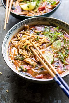 two bowls filled with noodles, vegetables and chopsticks on top of a table