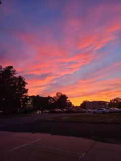 the sky is pink and blue as the sun sets in the distance with cars parked on the side of the road