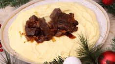 two pieces of meat on top of mashed potatoes in a white bowl surrounded by christmas decorations