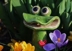 a frog statue sitting in the middle of some flowers