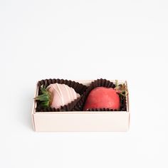 two chocolates in a white box with strawberries and an apple on the side