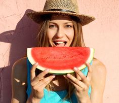 a woman holding a piece of watermelon in front of her face and smiling