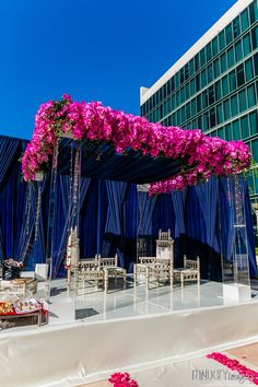 an outdoor wedding setup with purple flowers on the stage and blue drapes in the background