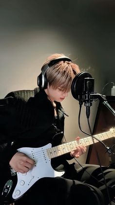 a young man sitting in front of a microphone while playing an electric guitar with headphones on