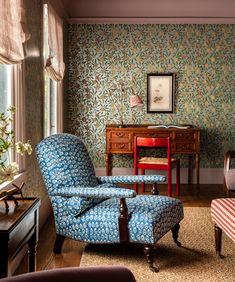 a living room with floral wallpaper and blue chairs in front of a desk area