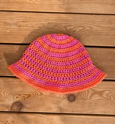 a pink and orange crocheted hat sitting on top of a wooden table