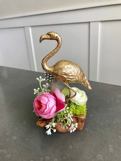 a gold flamingo sculpture sitting on top of a table next to flowers and greenery