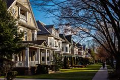 a row of houses with trees in the foreground and people walking on the sidewalk