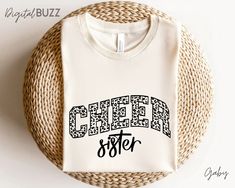 a white shirt with the word cheer sister on it sitting next to a wicker basket