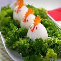 three eggs decorated like chickens sitting on top of some green leafy greens in a white plate