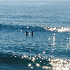 two surfers in the ocean on their surfboards with sun shining through the water