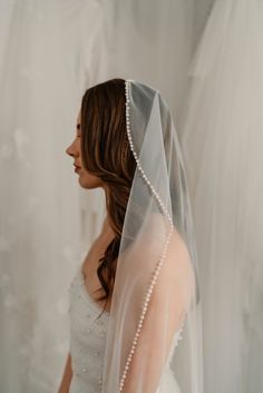 a woman wearing a wedding veil with pearls on the head and shoulder, standing in front of a white background