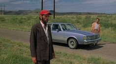 two men standing on the side of a road next to a car