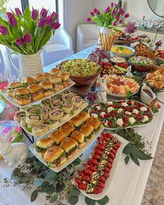 a table filled with lots of food and flowers on top of it, including sandwiches