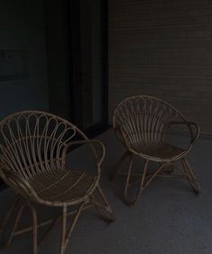 two wicker chairs sitting next to each other on the ground near a brick wall