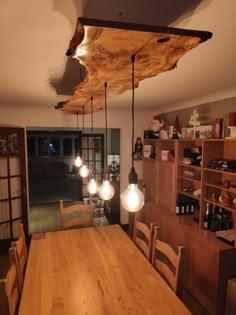 a wooden table with four lights hanging from it's ceiling and some shelves in the background