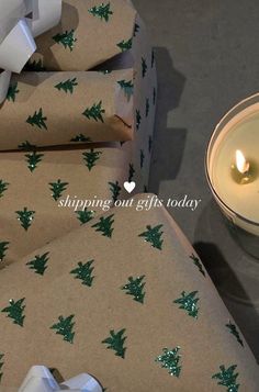 two wrapped presents sitting next to a lit candle on top of a table with wrapping paper