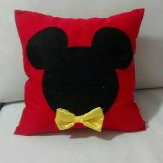 a mickey mouse pillow with a yellow bow tie on it's head, sitting on a white couch