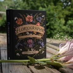 a book sitting on top of a wooden table next to a pink flower and greenery