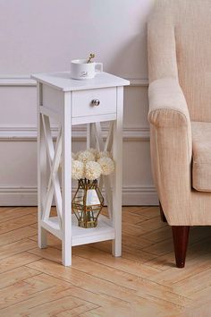 a white end table with flowers on it next to a couch and chair in a living room