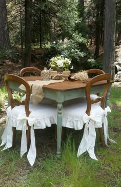 an old table and chairs are covered with white ruffled cloths in the woods