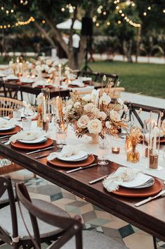 an outdoor dinner table set up with candles, plates and place settings for the guests