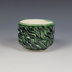 a green and white vase with wavy designs on the outside, sitting on a gray surface