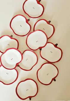 twelve red and white plates arranged in the shape of an apple, on a white surface