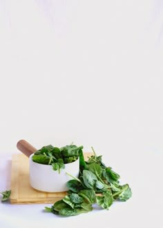 fresh basil leaves in a white bowl on a cutting board next to a wooden spoon